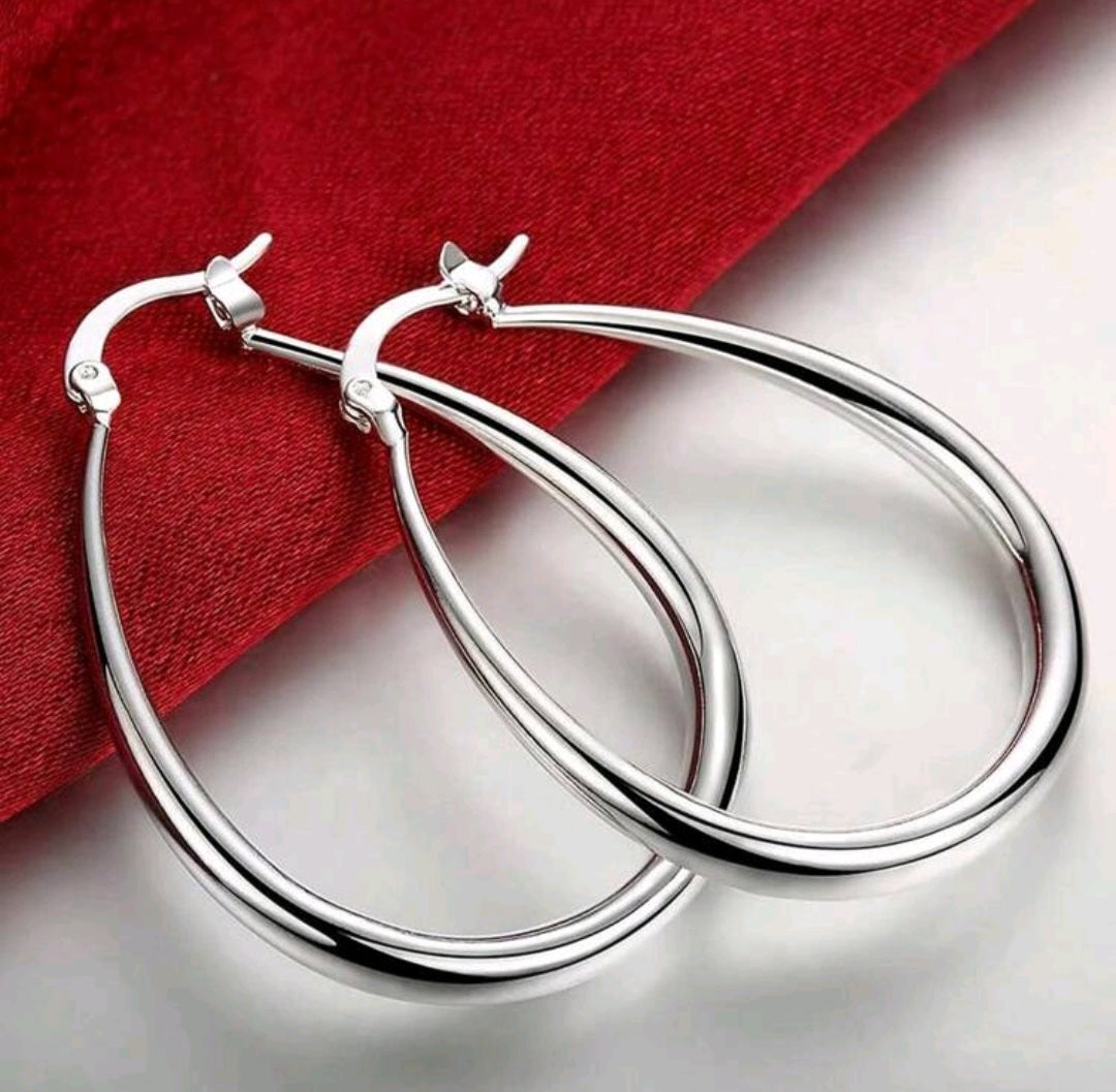 Silver hoop earrings on a reflective surface with a red fabric background
