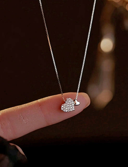 Heart-shaped pendant necklace held by a hand against a dark background