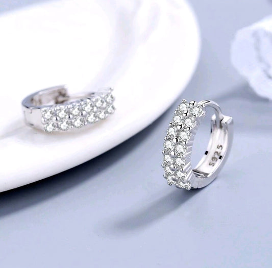 Silver hoop earrings with clear gemstones on a light gray surface.