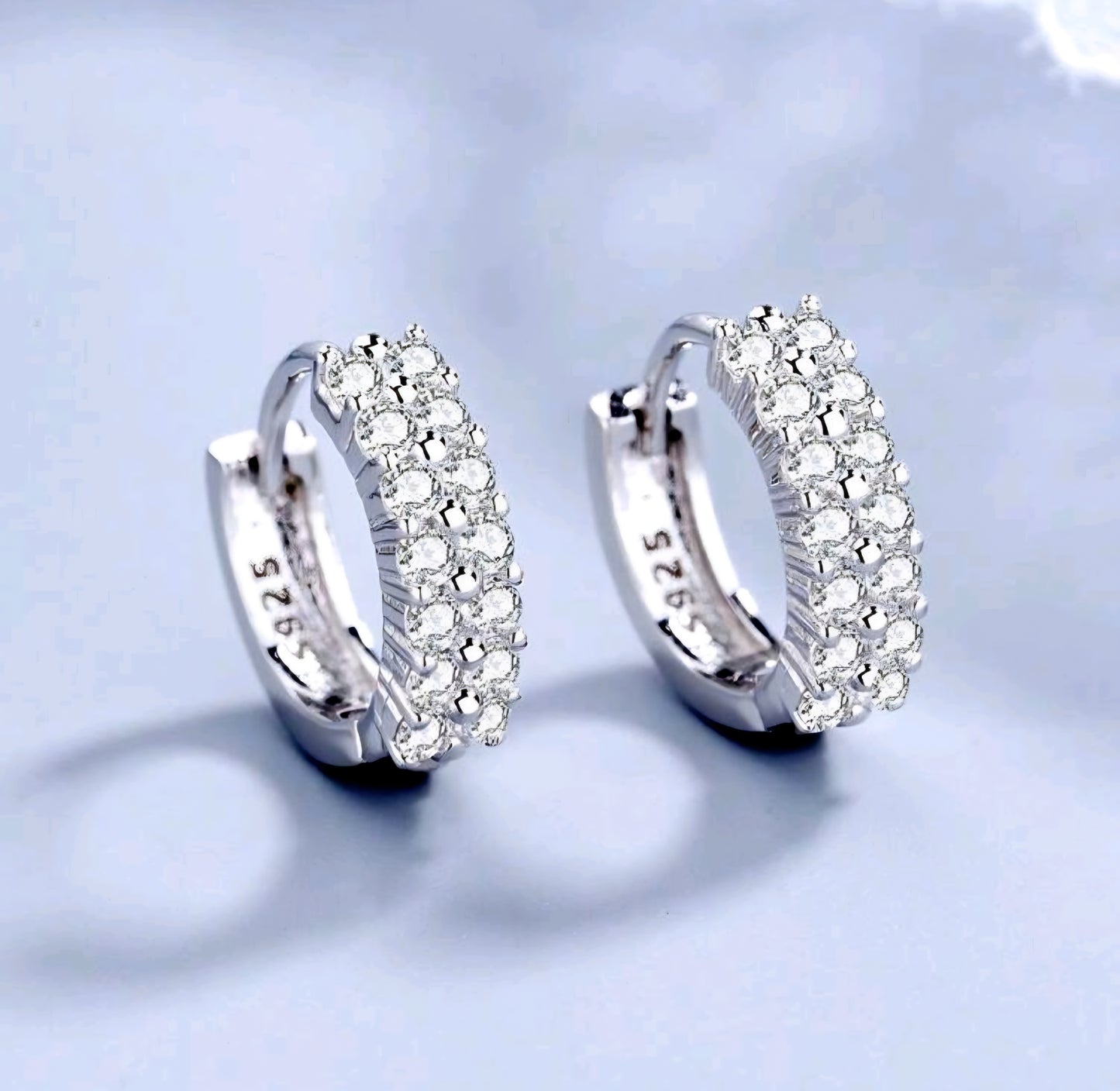 Silver hoop earrings with clear stones on a light blue background