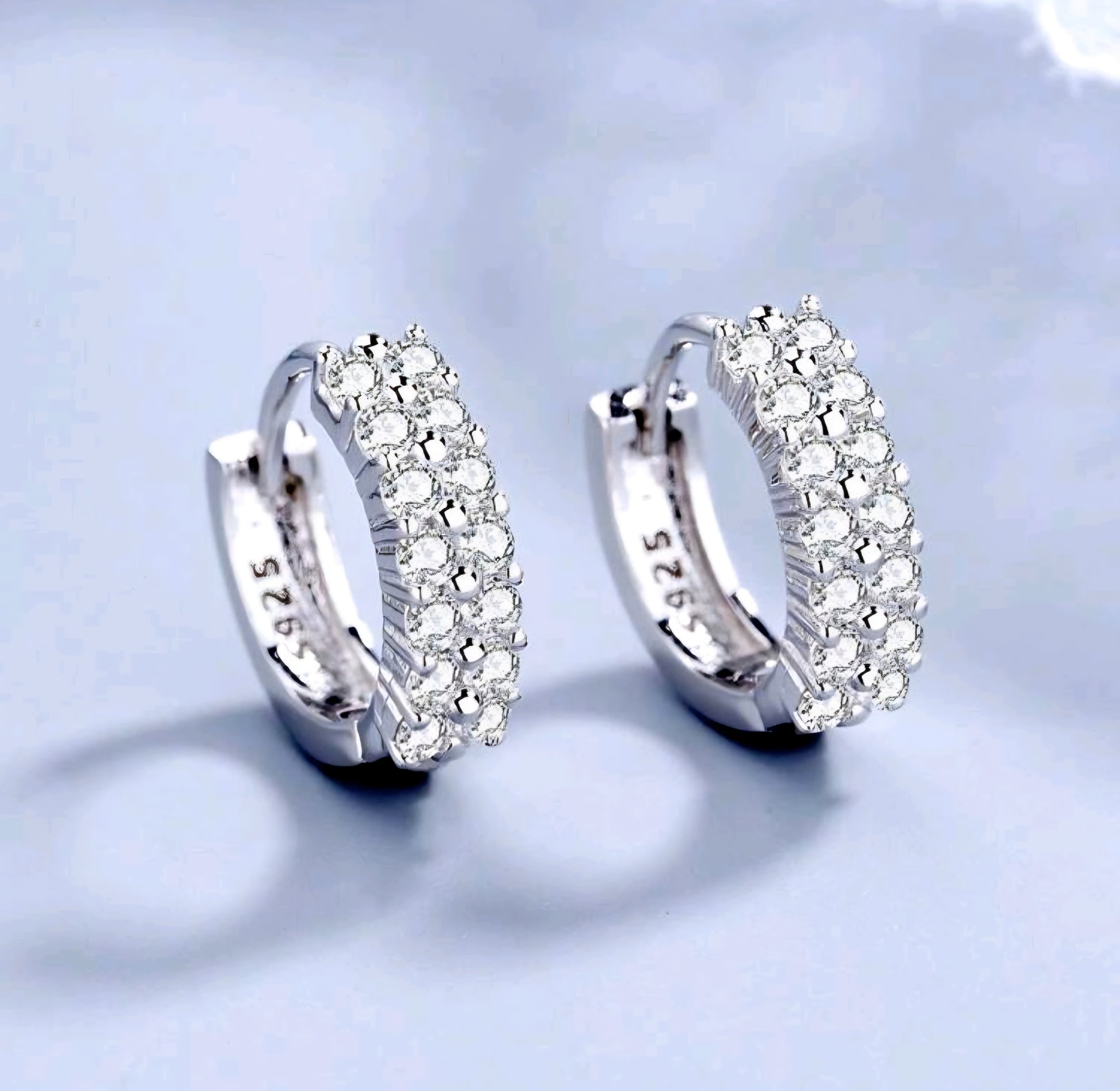 Silver hoop earrings with clear stones on a light blue background