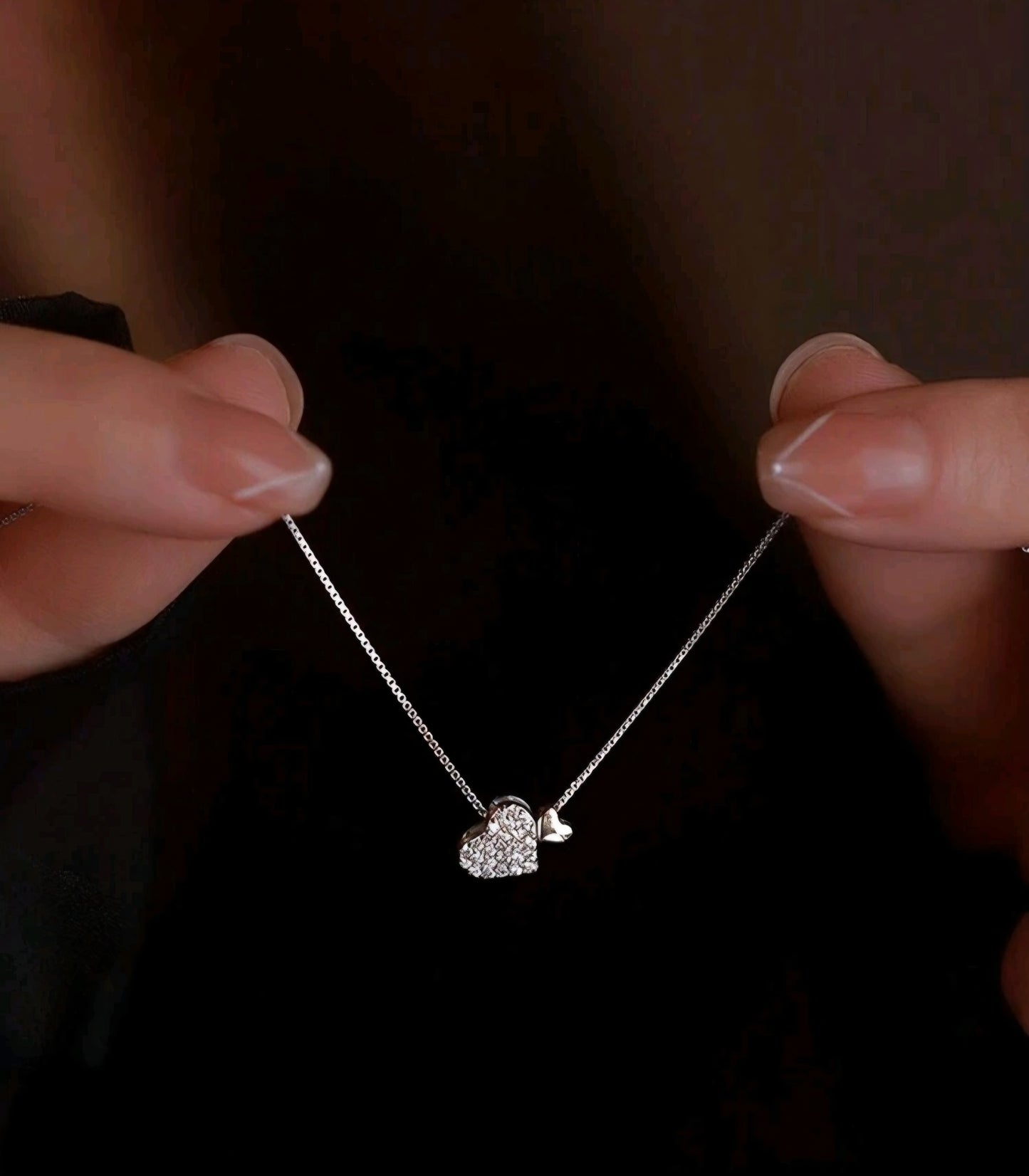 Close-up of a hand holding a delicate necklace with a small pendant against a dark background