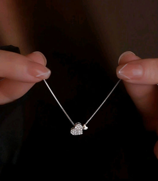 Close-up of a hand holding a delicate necklace with a small pendant against a dark background