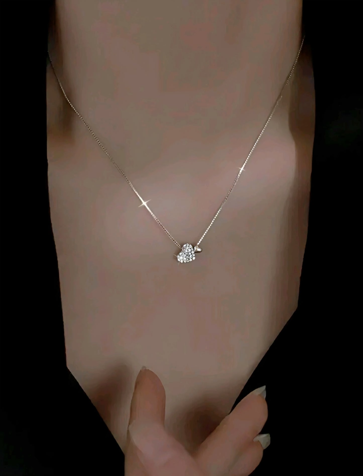 Silver necklace with a heart-shaped pendant on a person's wrist against a dark background